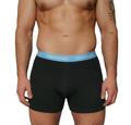 The image displays the upper body of an athletic man wearing the black boxer shorts by FRIEDENMEER, featuring a white 'FRIEDENMEER' text design on a light blue waistband, showcased and presented.