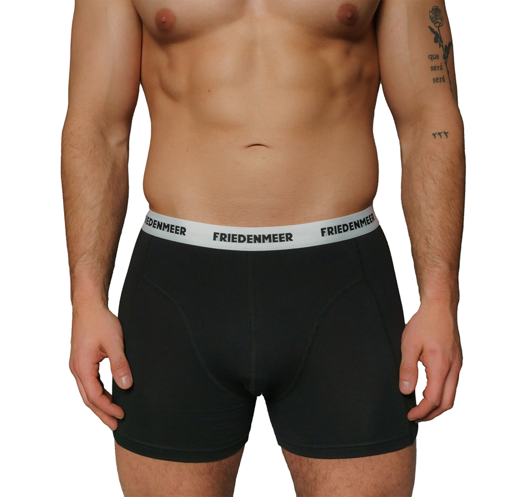 The image depicts the upper body of an athletic man that is wearing the black boxer shorts from the brand FRIEDENMEER, featuring a black 'FRIEDENMEER' text design on a white waistband, showcased and presented.