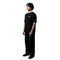 A model, showcases an elegant black T-shirt with the white brand name FRIEDENMEER across the chest, paired with matching black trousers and shoes, highlighting the brand's sleek elegance and luxury.