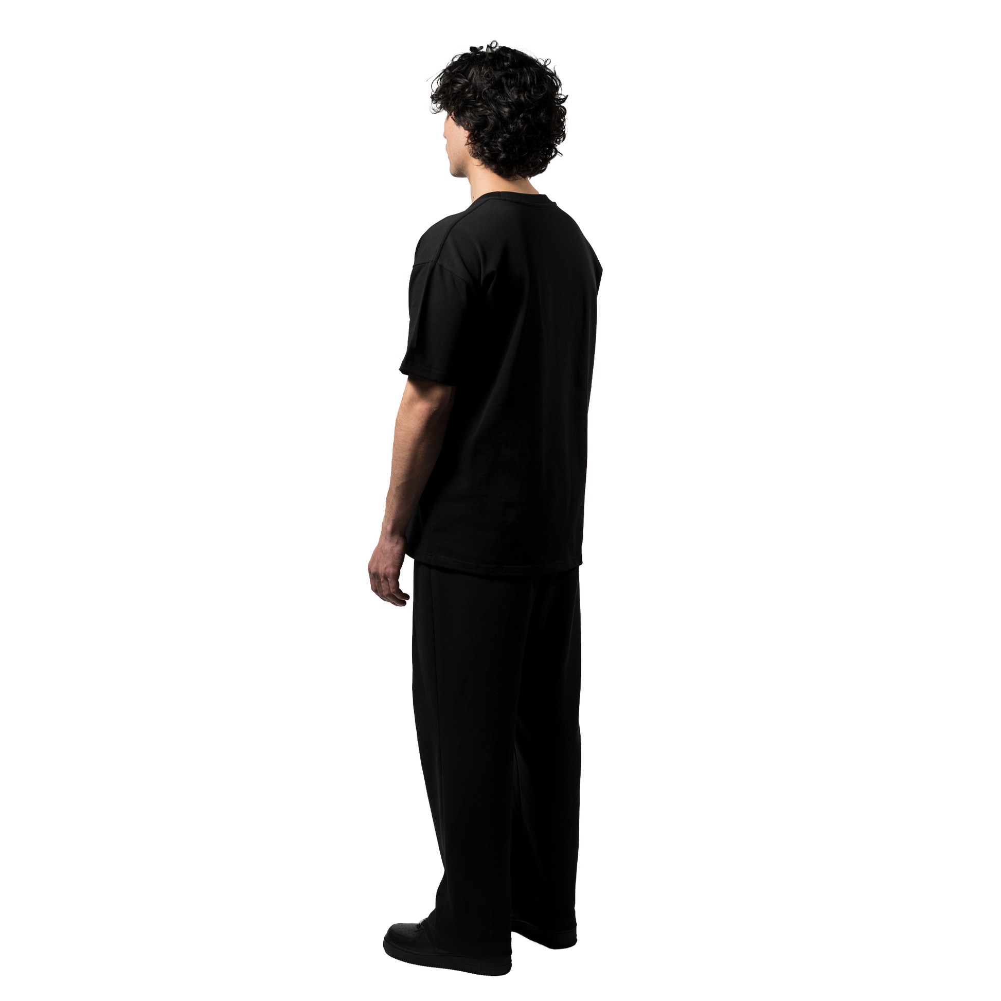 A model, showcases an elegant black T-shirt with the white brand name FRIEDENMEER across the chest, paired with matching black trousers and shoes, highlighting the brand's sleek elegance and luxury.