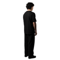 A model, with their face obscured, showcases an elegant black T-shirt with the white brand name FRIEDENMEER across the chest, paired with matching black trousers and shoes, highlighting the brand's sleek elegance and luxury.